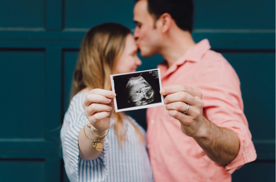 man-kissing-womans-forehead-white-holding-ultrasound-photo