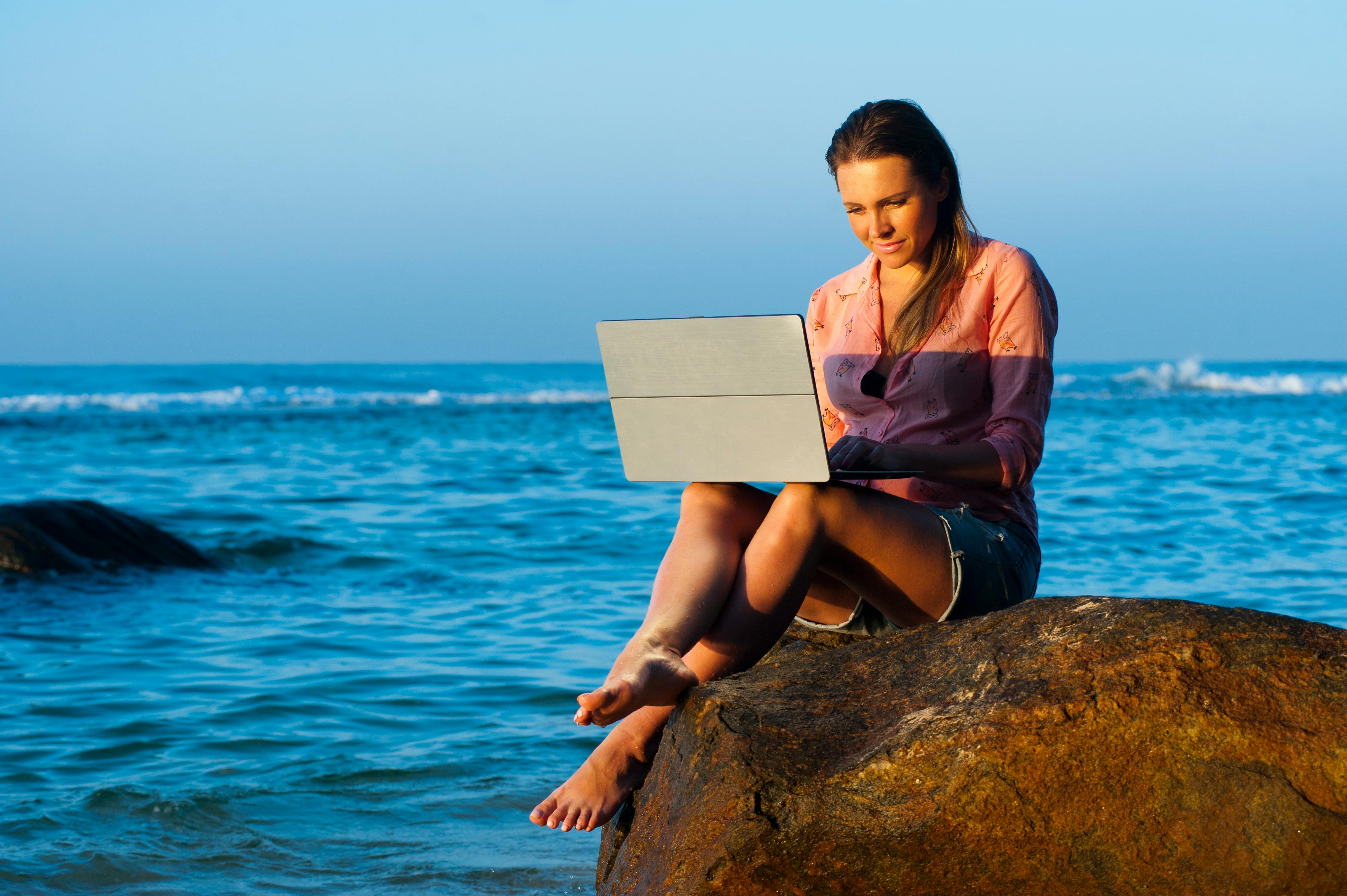 woman-sitting-on-brown-rock-while-using-laptop