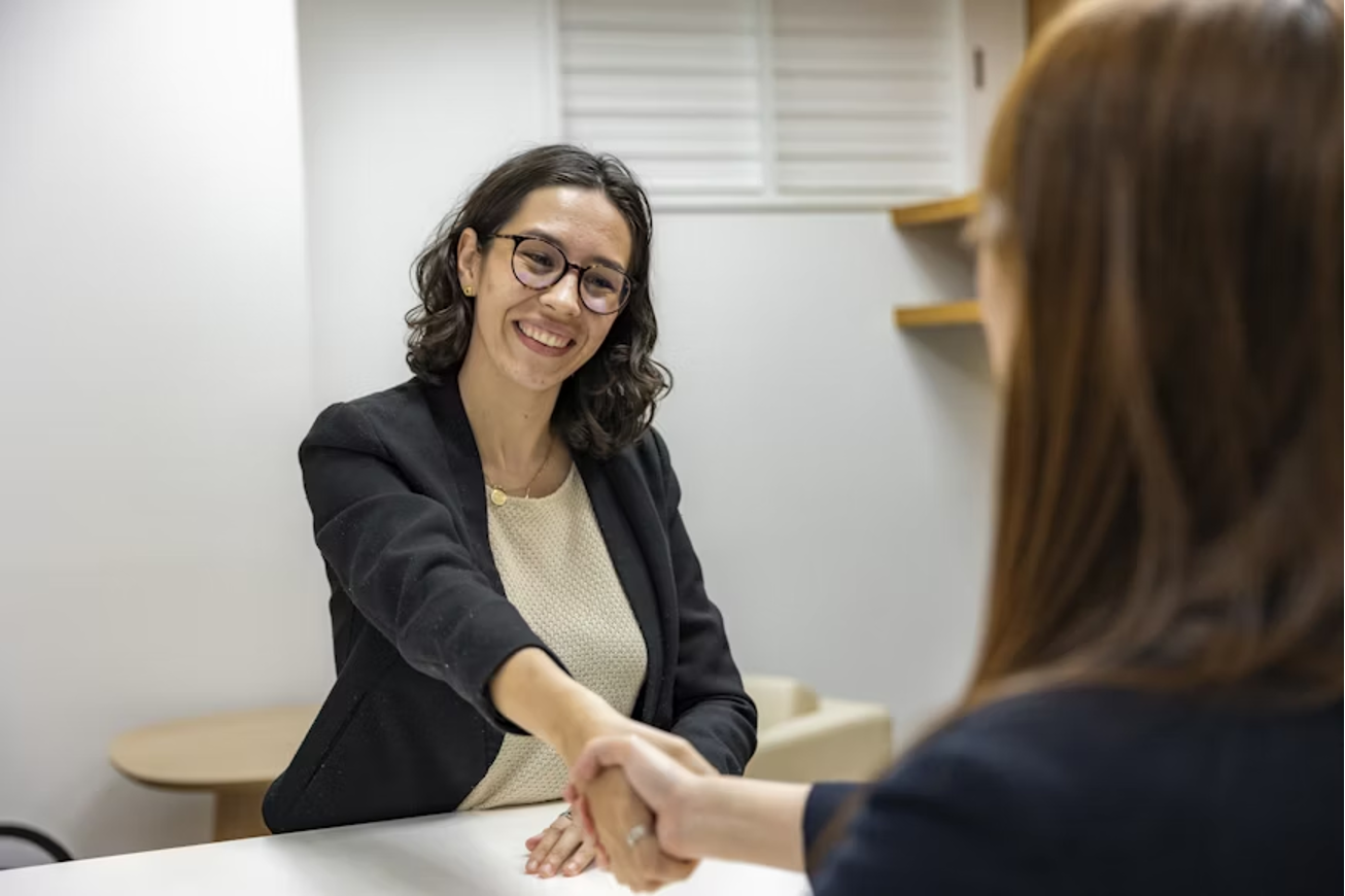 a-woman-shaking-hands-with-another-woman-sitting-at-a-table