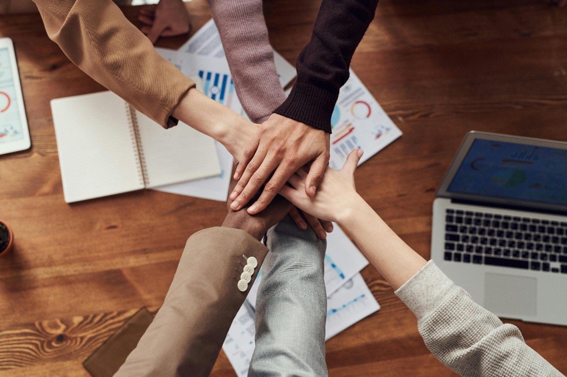 photo-of-people-stacking-hands-as-a-team-over-a-wooden-table